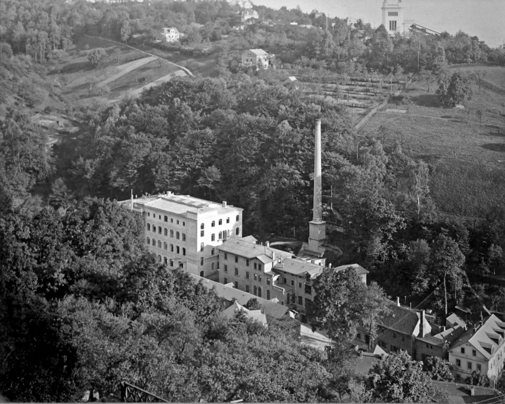 Die Tintenfabrik im Jahr des 75-jährigen Bestehens 1901 mit dem „Jubiläumshaus“ (links) und dem 35 Meter hohen Schornstein. Im Hintergrund ist die neu errichtete Bergstation der Schwebebahn zu erkennen. Foto: Jubiläumsalbum (Archiv Leonhardi-Museum)