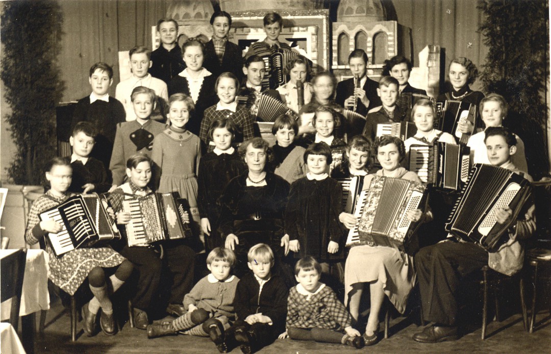 Therese Visino, sie wurde zu ihrer Zeit noch mit „Fräulein“ angesprochen, war selbständige Musiklehrerin und gab in ihrer Wohnung (Bautzner Landstraße 72, Erdgeschoss) Unterricht in Klavier, Violine und Akkordeon. Die Aufnahme stammt etwa aus dem Jahre 1955. Meine Schwester und ich hatten bei ihr Klavierunterricht. Beliebt (mehr bei den Eltern) waren die Schülerkonzerte, die im Parkhotel Weißer Hirsch stattfanden (Blauer Salon). Frl. Visino, die gelegentlich auch in der Bühlauer Kirche als Organistin aushalf, hatte etwas Geniales und Großzügiges an sich, gab Unterricht manchmal im Morgen- bzw. Hausmantel, also „eine wahre Künstlerin“. Sie heiratete in späteren Jahren und dann erst widmete sie sich der „Naiven Malerei“. Text und Foto: Dr. Lindenau