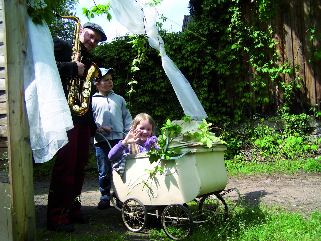 Inspiriert vom Kinderbuch „Der kleinen Hävelmann“ freut sich Vater Tietke mit seinen beiden Kindern, Rosina und Robinson, mittels historischem Kinderwagen die Reise durch das offene Fenster mit wehenden Gardinen, in ein Land der Elbhangfest-Tagträume anzutreten. Foto: J & KS