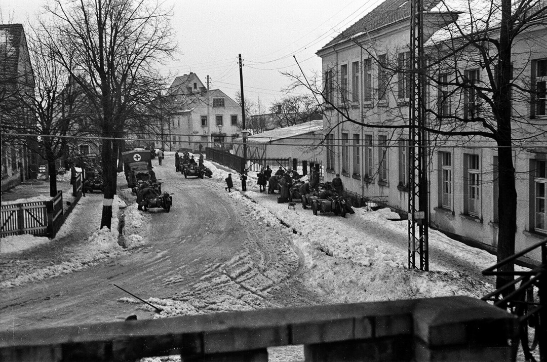 Wehrmachtssoldaten auf der Hutbergstraße zwischen Gasthof und Schule um 1943. Im Hintergrund auf dem Schulhof ist ein großes Zelt zu sehen, worin vermutlich Soldaten einquartiert waren. Dazwischen läuft ein Kind zur Schule.  Foto: Sammlung Karl Richter